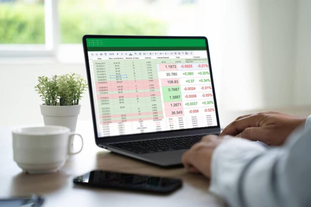A person analyzes a financial spreadsheet on a laptop, with a potted plant and coffee cup nearby, in a well-lit room.