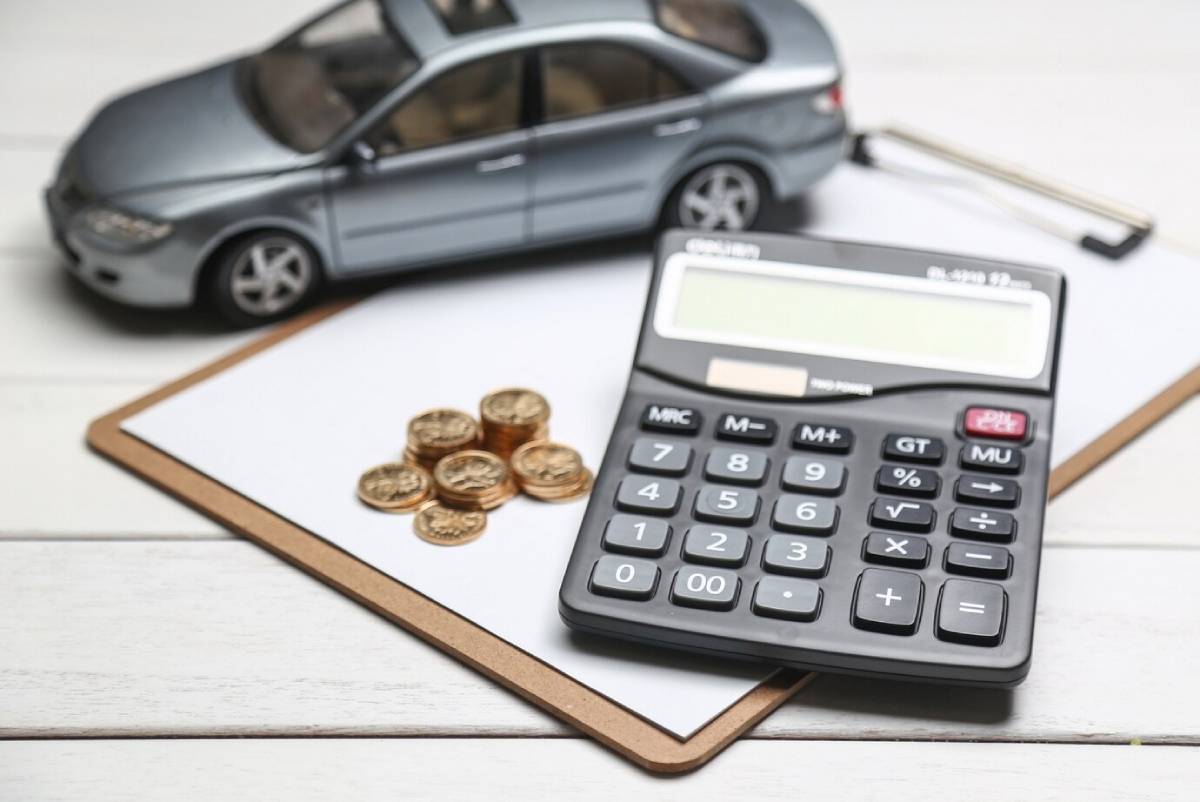  A toy car, calculator, and stacks of coins on a clipboard, symbolizing budgeting for vehicle expenses.