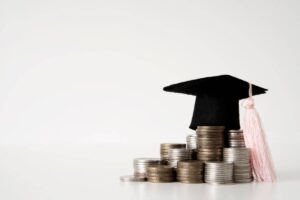 A graduation cap rests atop a stack of coins, symbolizing the cost of education and financial investment in learning.