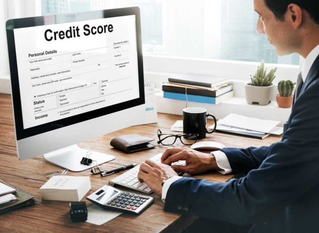 A person in a suit accesses a credit score form on a computer, surrounded by office supplies and plants on a desk.