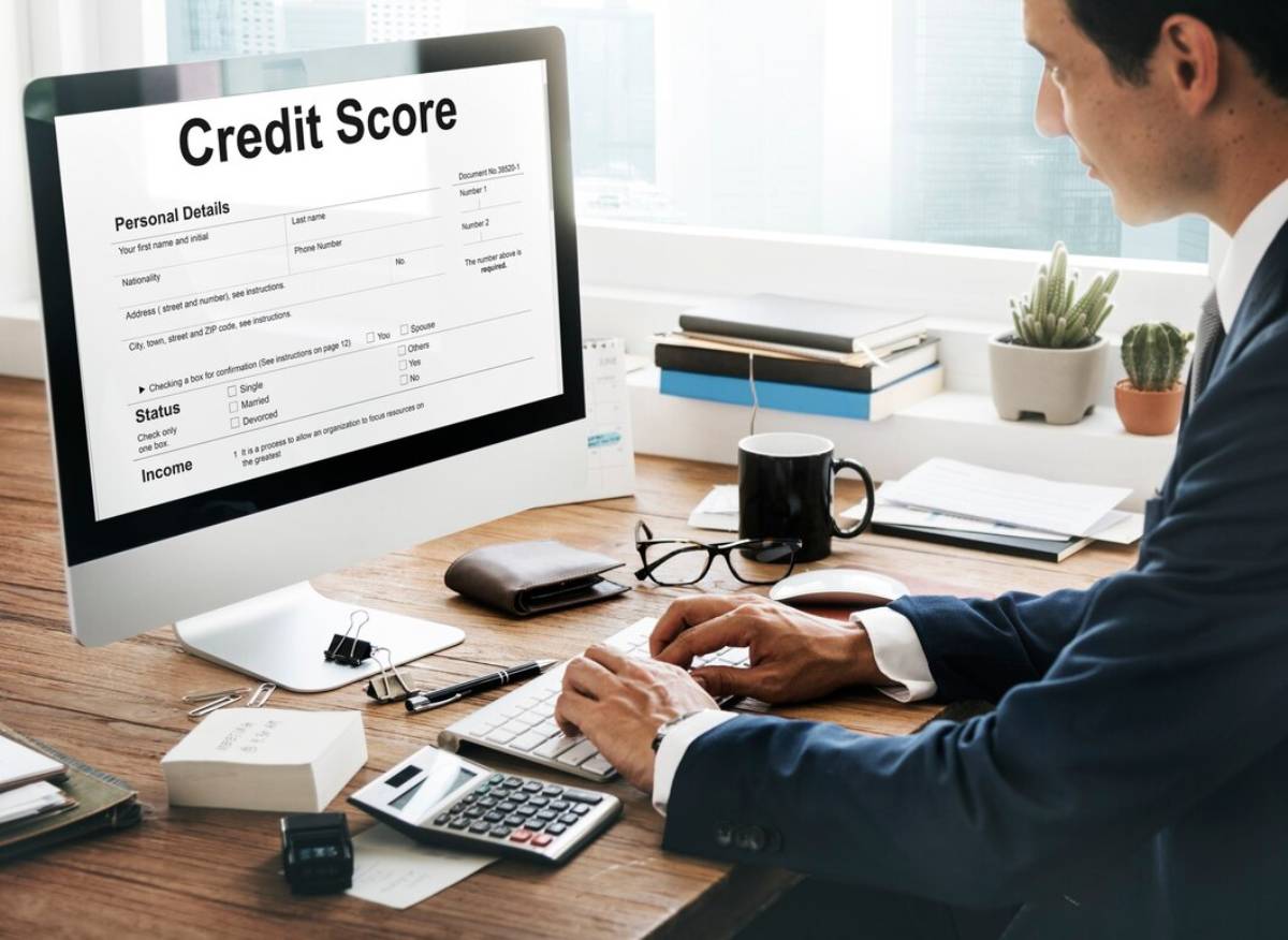 A person in a suit accesses a credit score form on a computer, surrounded by office supplies and plants on a desk.