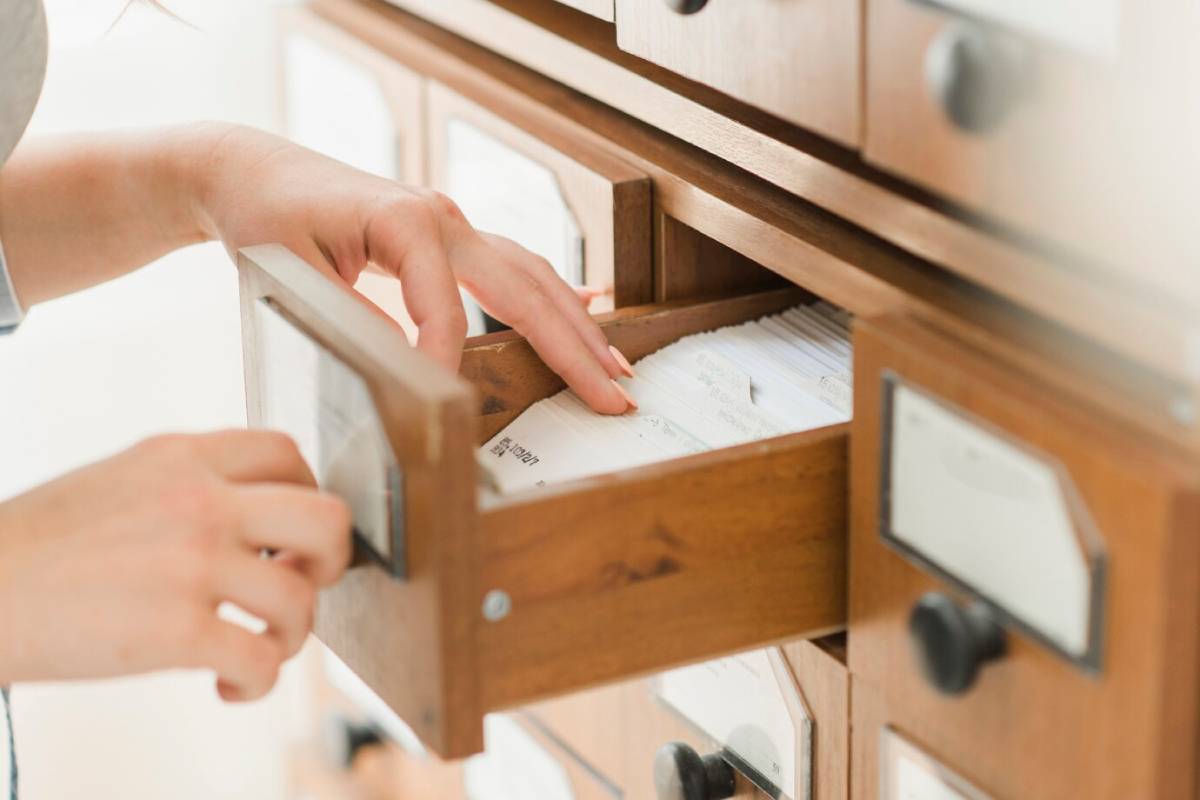 A hand reaches into a wooden drawer filled with index cards, highlighting a vintage filing system for organizing information.