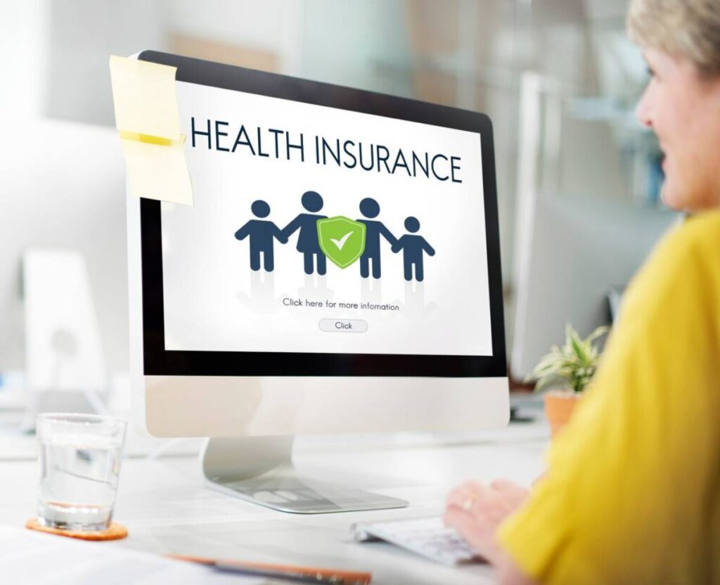 A person in a yellow shirt views a computer screen displaying "Health Insurance" with icons of family figures and a checkmark.
