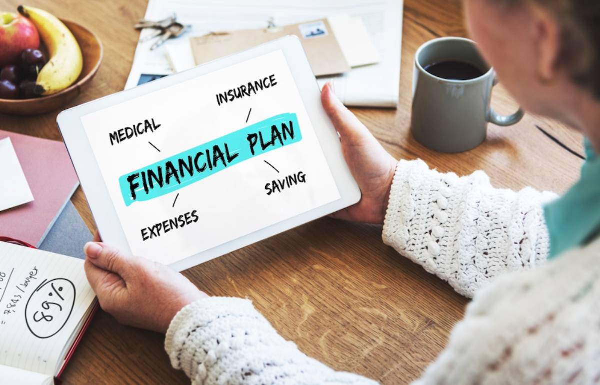 A person holding a tablet displaying a financial plan with key elements: medical, insurance, expenses, saving, surrounded by office supplies. 