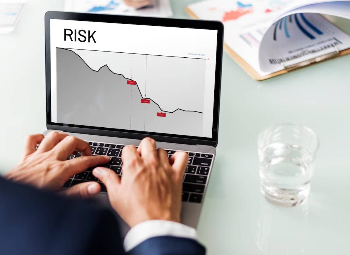A person analyzes a risk graph on a laptop, highlighting a downward trend, with a glass of water visible on the table. 