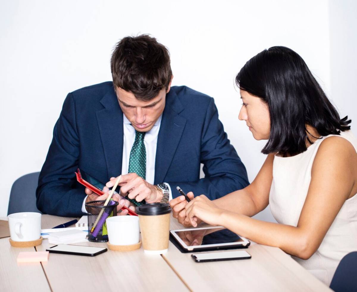 A professional discussion at a table with coffee, notebooks, and digital devices, focusing on collaboration between two individuals. 