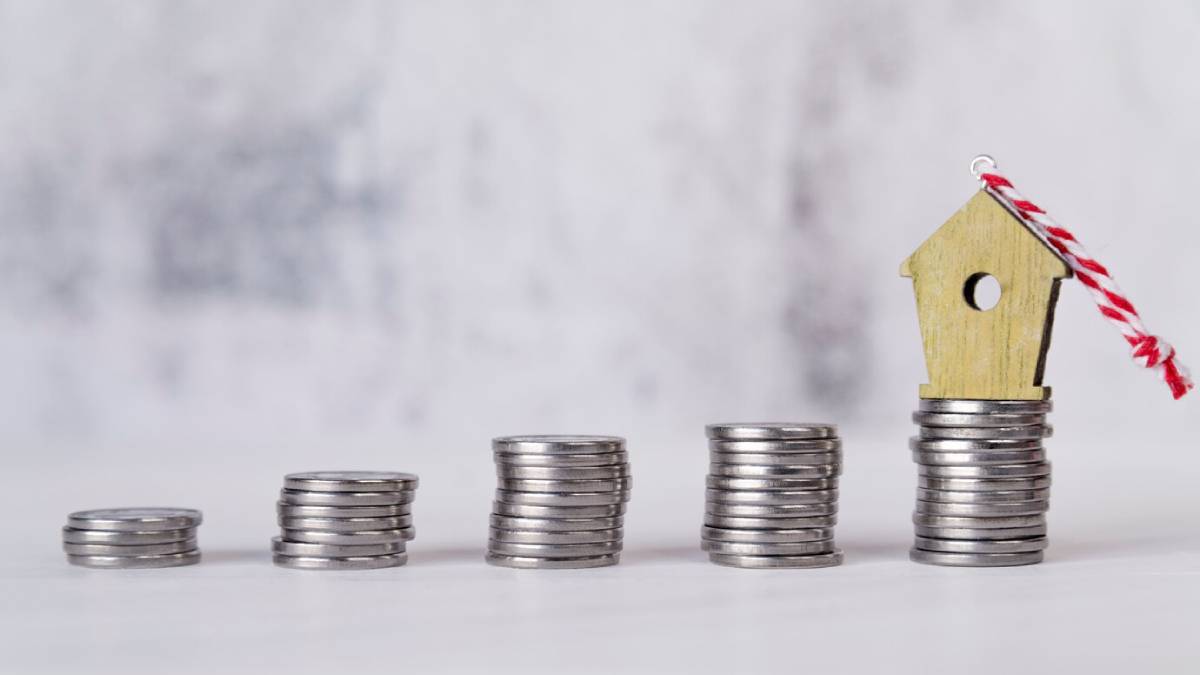 Stacks of coins increasing in height, topped with a small wooden house, symbolizing savings and investment in real estate. 