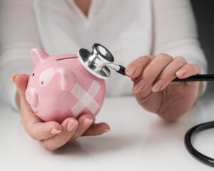 A person examines a pink piggy bank with a stethoscope, symbolizing financial health, with a bandage patch on the piggy's side.