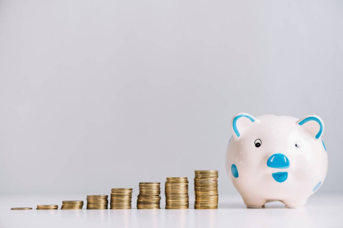 A cute white piggy bank with blue accents beside a growing stack of gold coins, representing savings and financial growth.