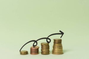 Stacks of coins with a curved arrow indicating upward growth or investment success against a light green background.
