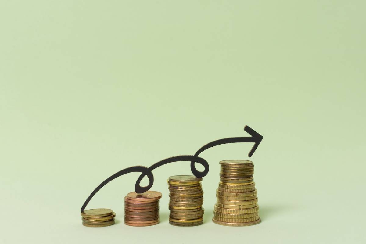 Stacks of coins with a curved arrow indicating upward growth or investment success against a light green background.