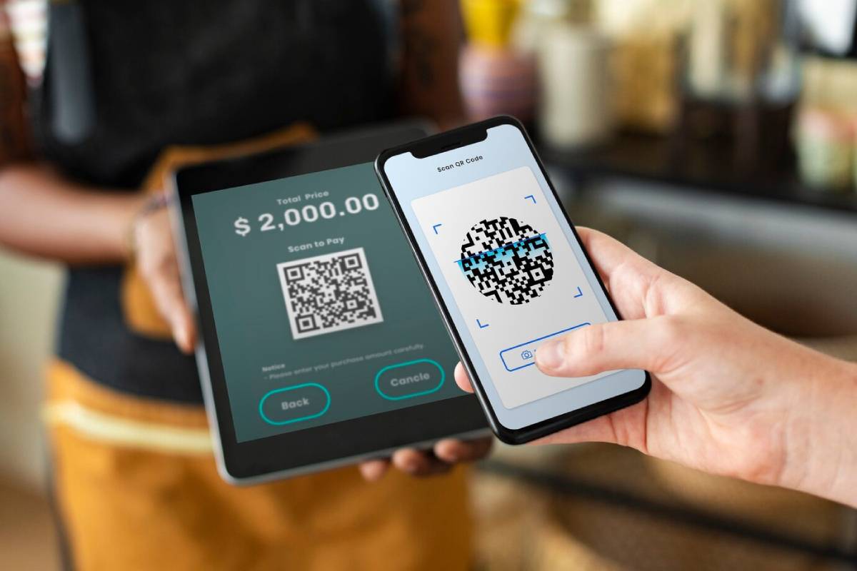 A person scanning a QR code on their phone to pay $2,000 displayed on a tablet, indicating a digital payment transaction.