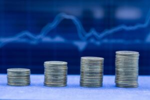 Stacks of coins arranged in ascending order with a blue financial chart backdrop, illustrating growth and investment trends.