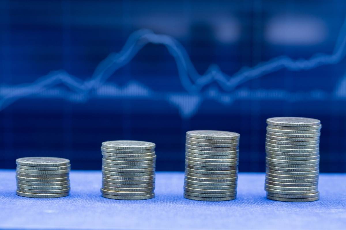 Stacks of coins arranged in ascending order with a blue financial chart backdrop, illustrating growth and investment trends.