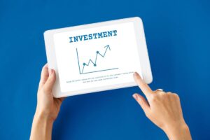 A hand holding a tablet displaying a graph with an upward trend, titled Investment, against a blue background.