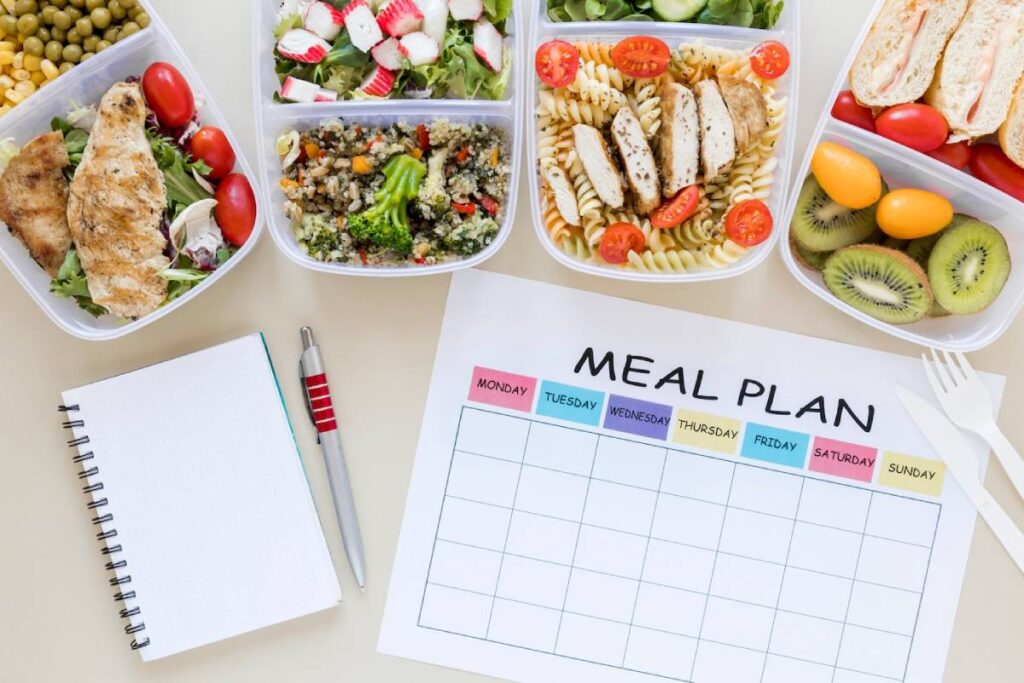 A meal prep setup featuring assorted healthy foods in containers, with a blank meal plan sheet and a notebook with a pen beside it.