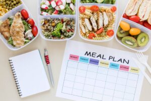 A meal prep setup featuring assorted healthy foods in containers, with a blank meal plan sheet and a notebook with a pen beside it.