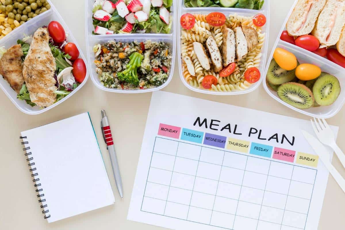 A meal prep setup featuring assorted healthy foods in containers, with a blank meal plan sheet and a notebook with a pen beside it.