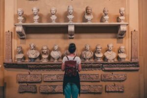 A visitor admires a wall display of classical marble busts, framed by decorative carvings in a softly lit museum setting.